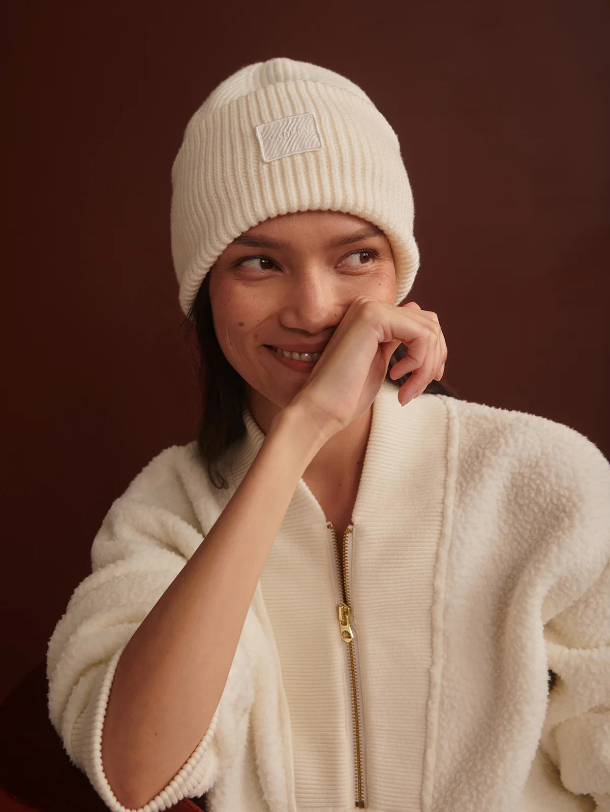 Person wearing a cream beanie and jacket against a brown background