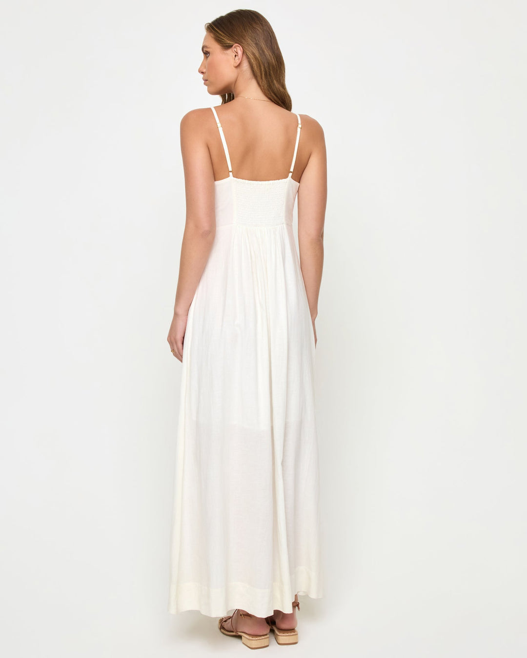 Back view of a model wearing the LSPACE Mabel Maxi Dress in cream, featuring thin spaghetti straps, an open back with gathered waist detail, and a flowing full-length silhouette.