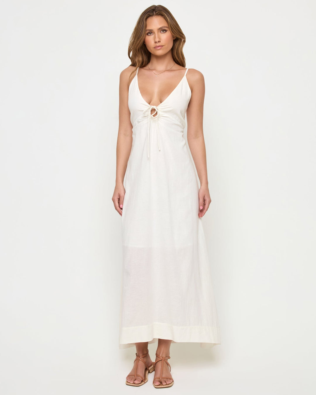 Front view of a model wearing the LSPACE Mabel Maxi Dress in cream, featuring thin spaghetti straps, a deep V-neckline with ruched drawstring tie at the bust, and a flowing full-length silhouette.