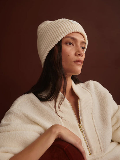 Woman wearing a cream beanie and jacket against a brown background