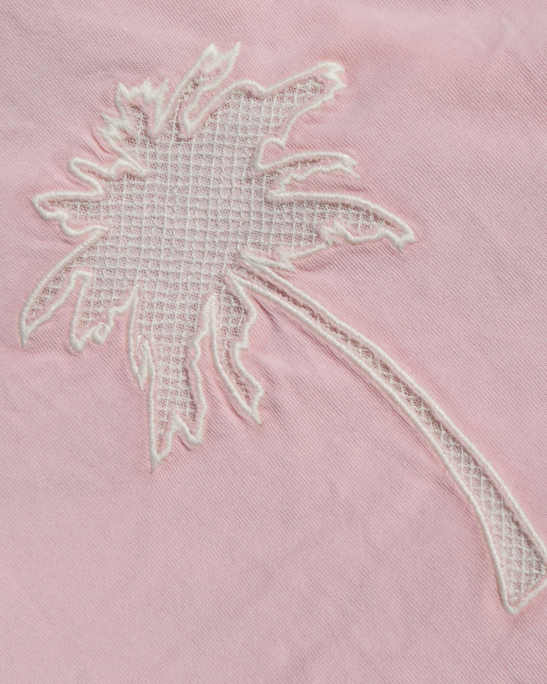 A close-up of a light pink fabric featuring a white embroidered palm tree motif.