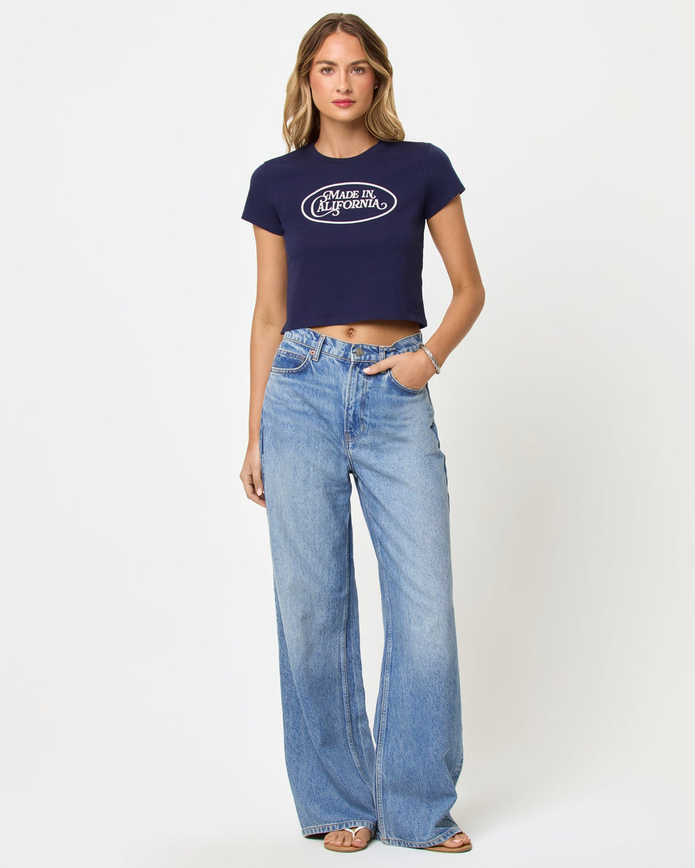 Front view of model wearing the LSPACE Merci Baby Tee in made in California midnight blue, a cropped navy fitted tee with a white graphic print on the chest.