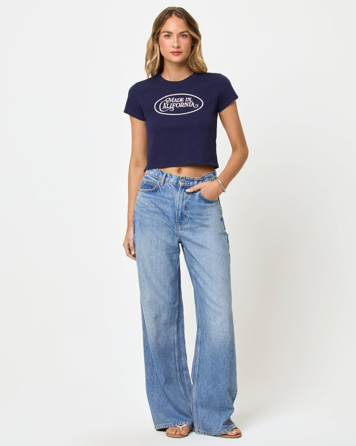 Front view of model wearing the LSPACE Merci Baby Tee in made in California midnight blue, a cropped navy fitted tee with a white graphic print on the chest.