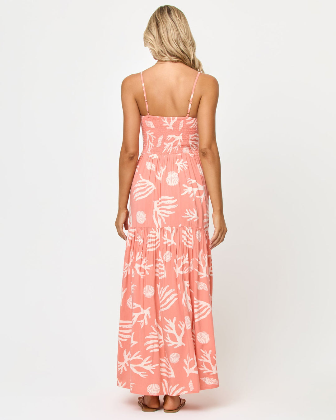 Back view of a model wearing the LSPACE Mallorca Dress in Shell Or High Water, showing the smocked back bodice and tiered maxi skirt in the coral shell and reef print.
