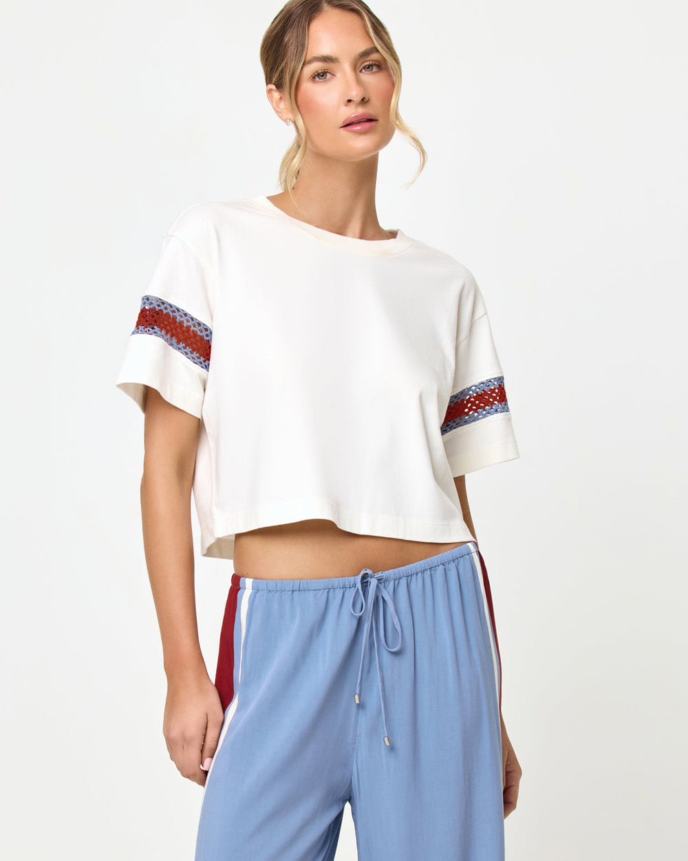 Cropped torso and waist-up studio view of the Core Top in Cream-Chambray-Fig, a cream short-sleeve boxy crop tee with blue and burgundy chevron crochet trim at the sleeve hems, styled with chambray blue wide-leg stripe pants with a drawstring waist.