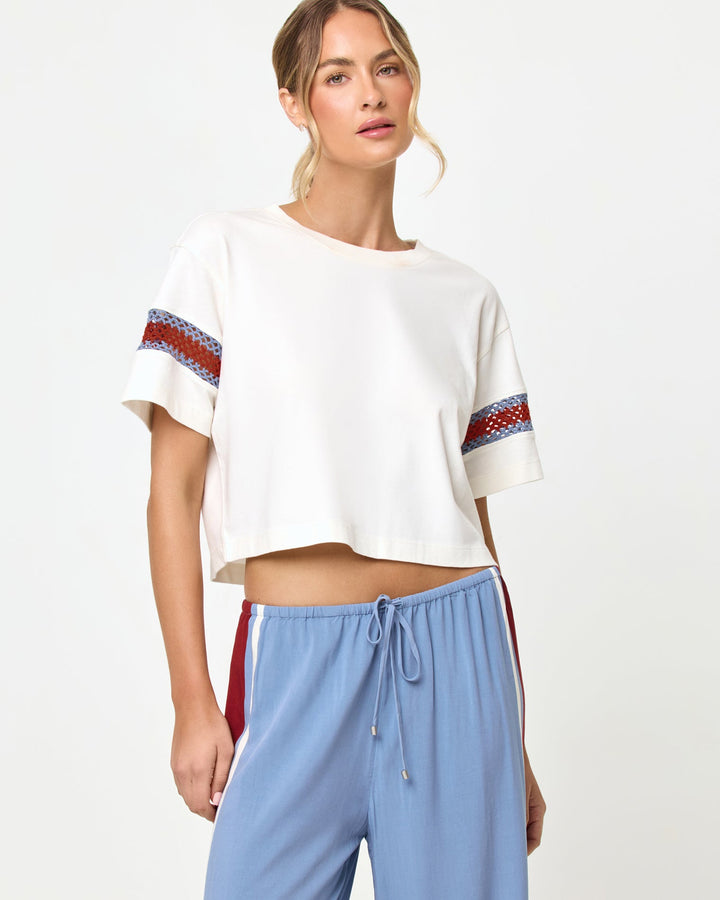 Cropped torso and waist-up studio view of the Core Top in Cream-Chambray-Fig, a cream short-sleeve boxy crop tee with blue and burgundy chevron crochet trim at the sleeve hems, styled with chambray blue wide-leg stripe pants with a drawstring waist.