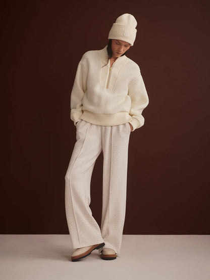 Person wearing a cream-colored sweater and pants with a white beanie against a dark brown background