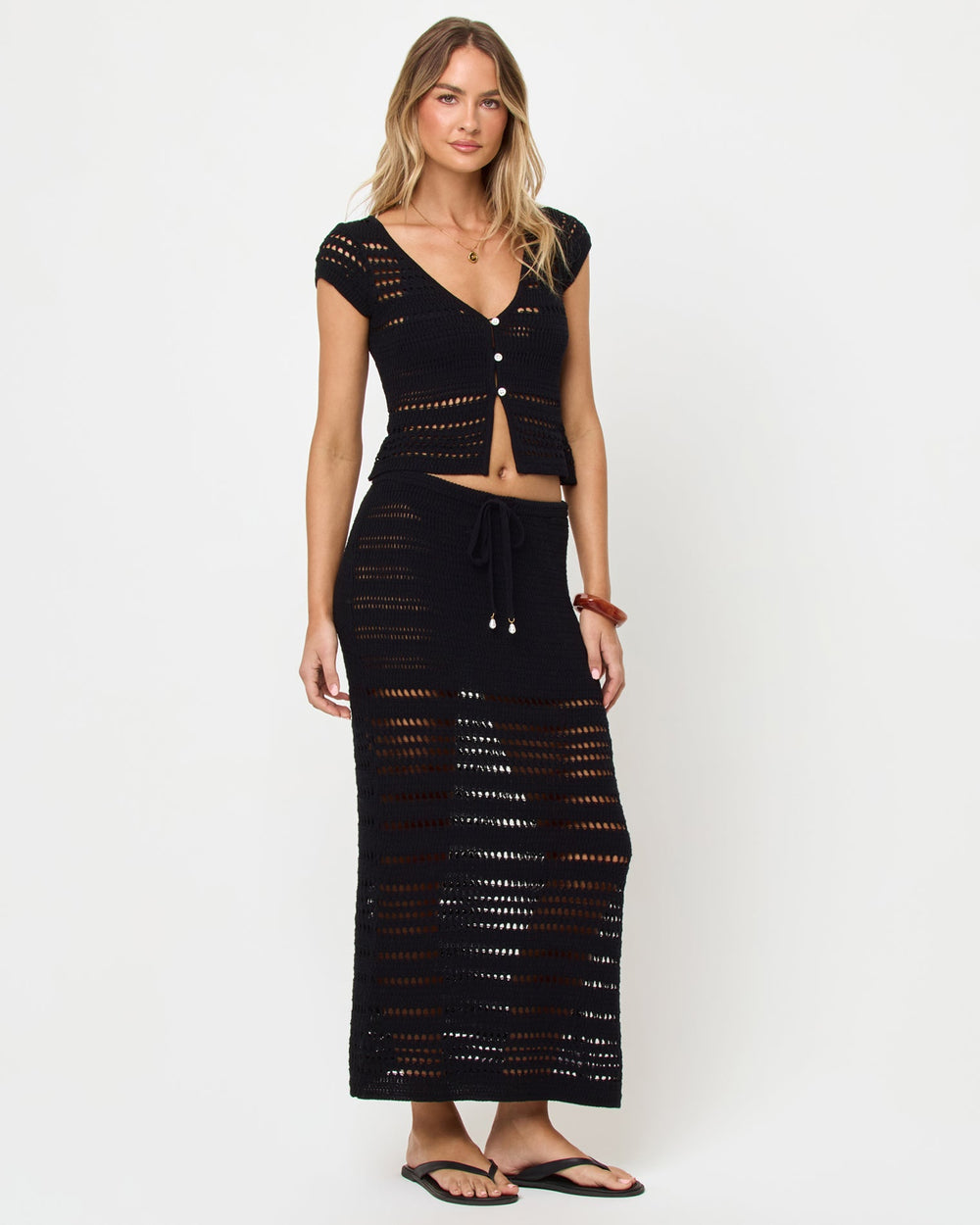 Side view of model wearing the LSPACE Tula Top in black, a semi-sheer crochet cropped top with cap sleeves with the mathcing Skirt.
