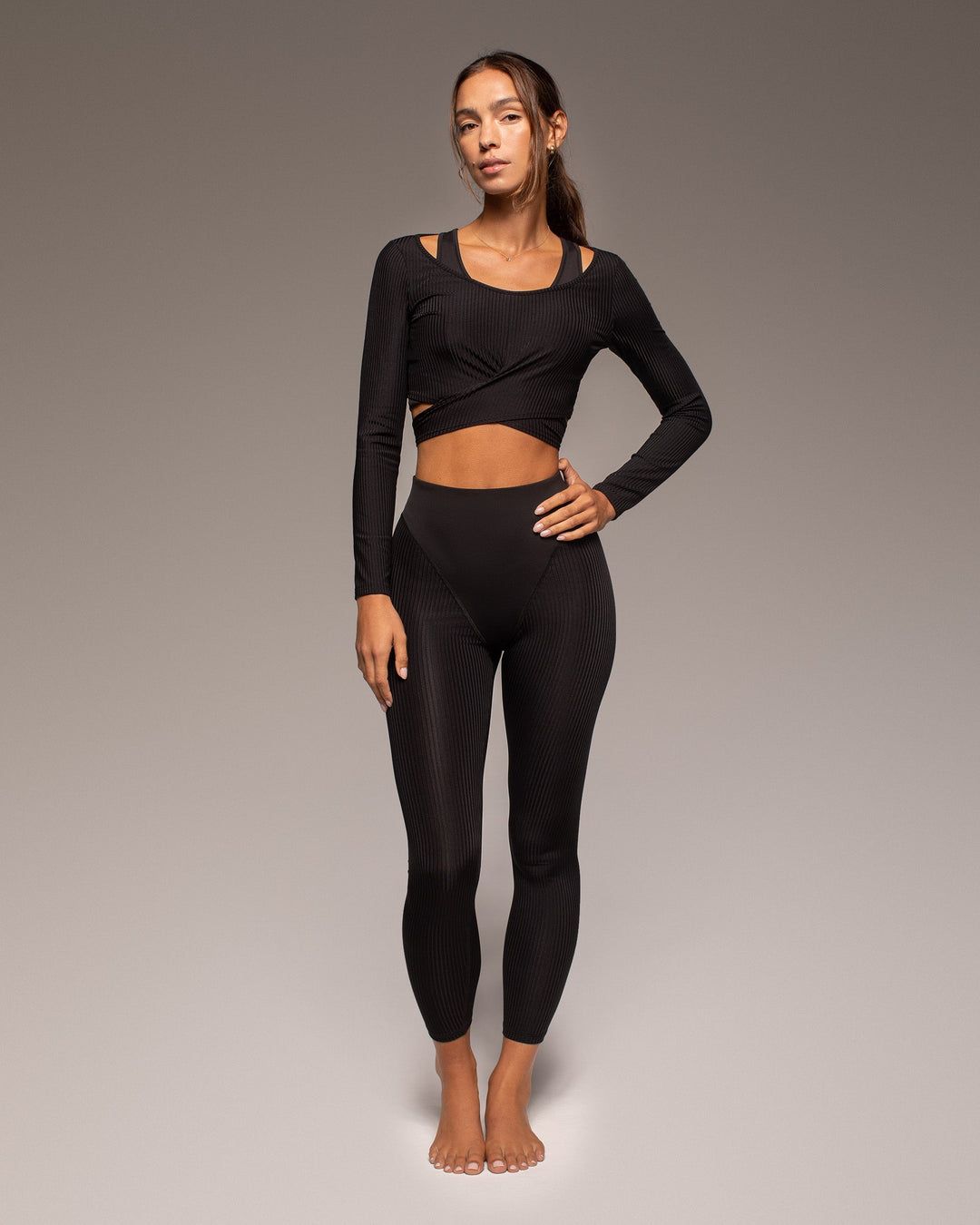 Woman wearing a black long-sleeve crop top and leggings on a gray background