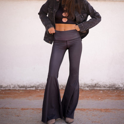Person wearing a dark jacket, crop top, and flared pants against a plain background