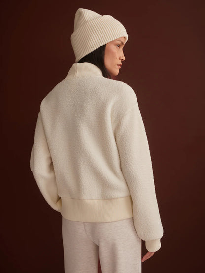 Person wearing a cream-colored outfit with a beanie against a dark brown background