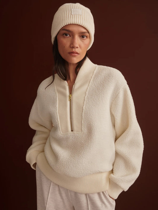 Person wearing a cream-colored fleece pullover and beanie against a dark background