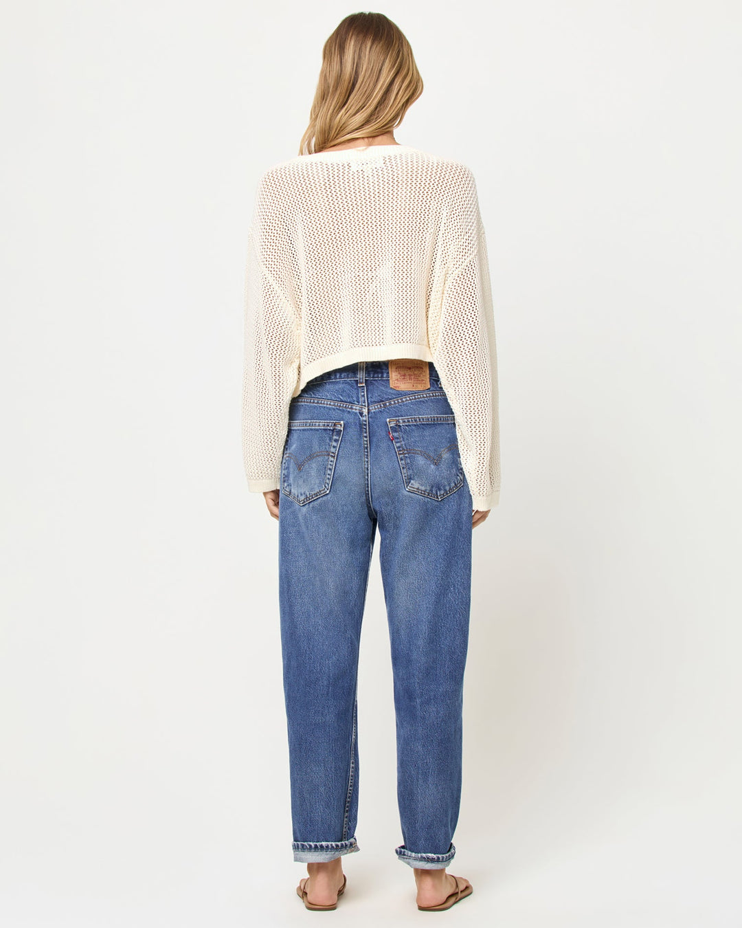 Back view of a model wearing the LSPACE Island Time Sweater in Cream, styled with jeans, showing the open-knit crochet construction and relaxed fit.