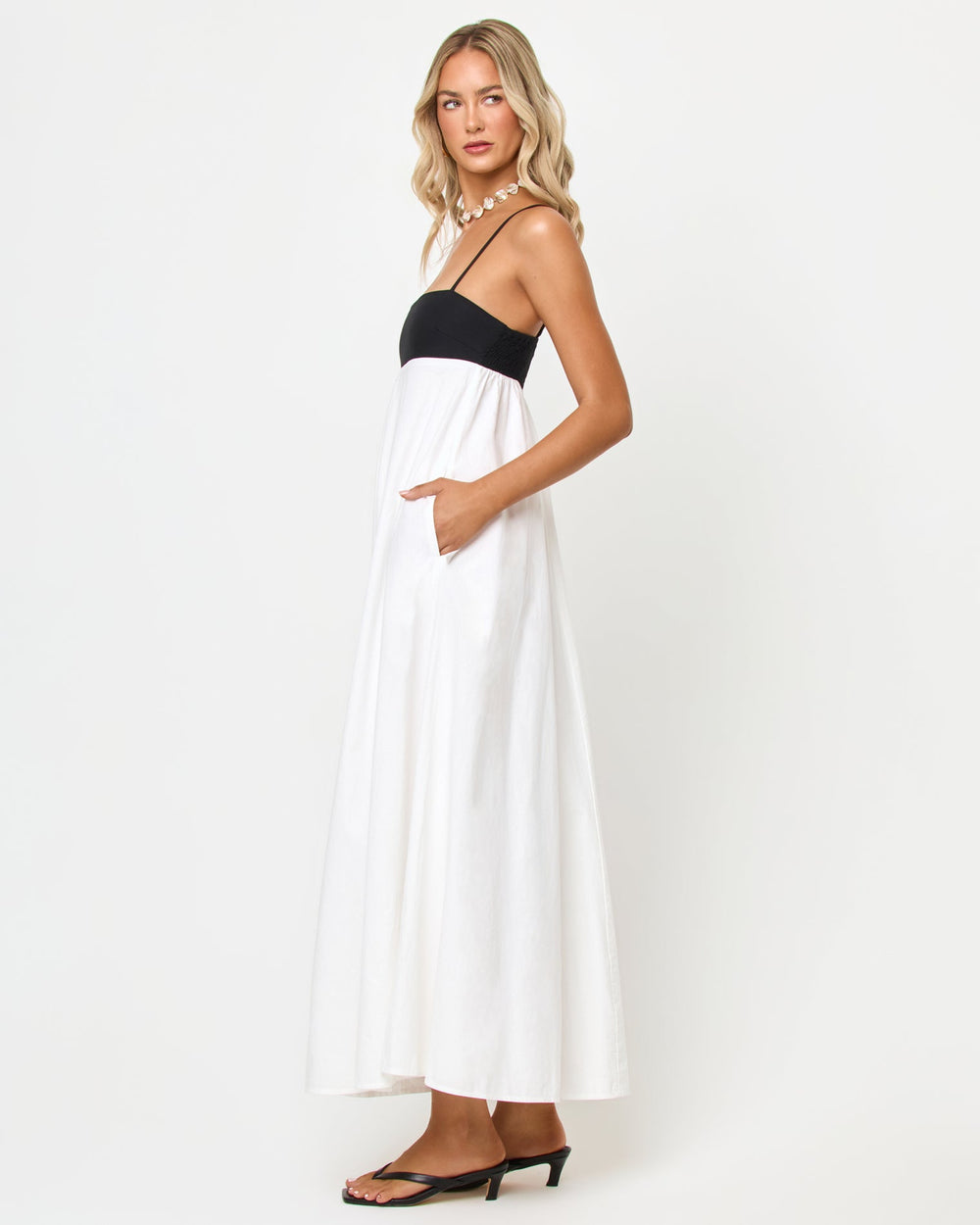 Side view of a model wearing the LSPACE Raveena Dress in black-cream, showing the empire-waist silhouette with a black bodice, spaghetti straps, and a flowing cream maxi skirt.