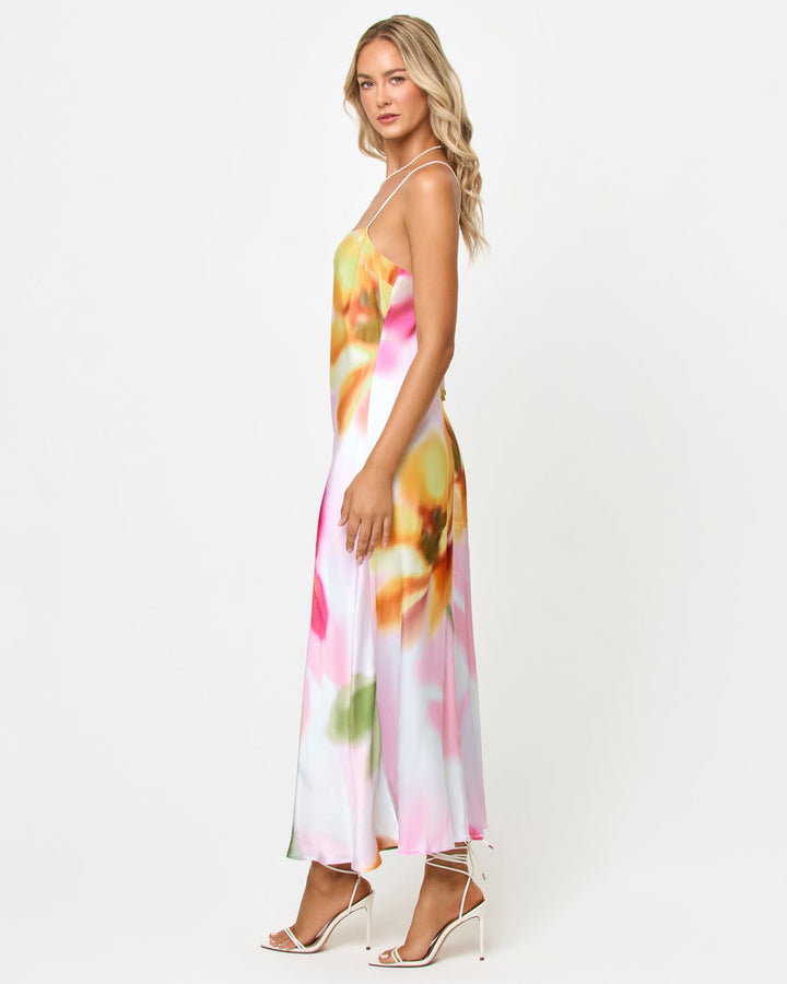 Side view of a model wearing the LSPACE Gabby Maxi in soft focus, showing the bias-cut satin silhouette and strappy back detail with the blurred floral print.