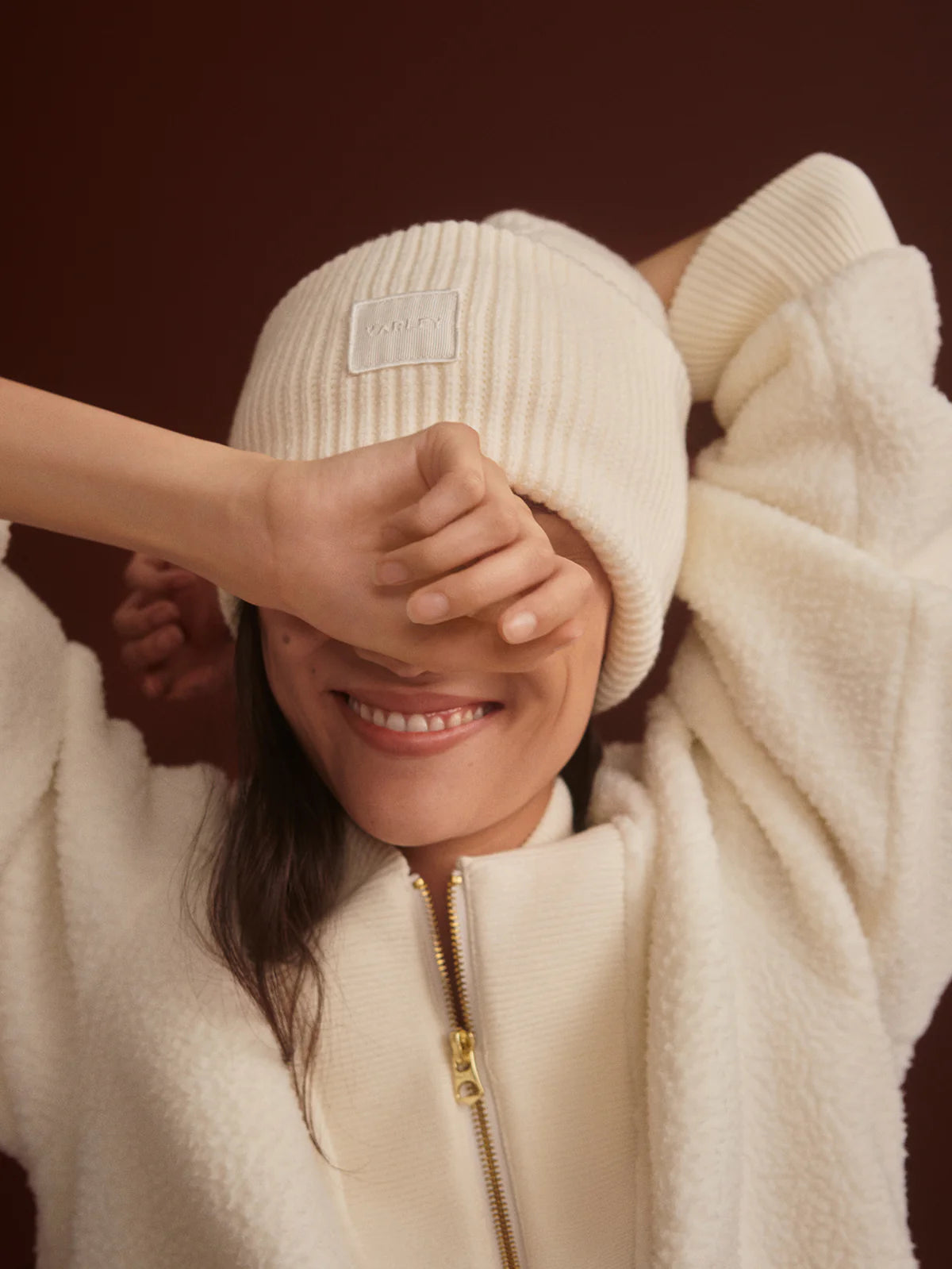 Person wearing a cream-colored knit hat and coat with a visible brand logo.