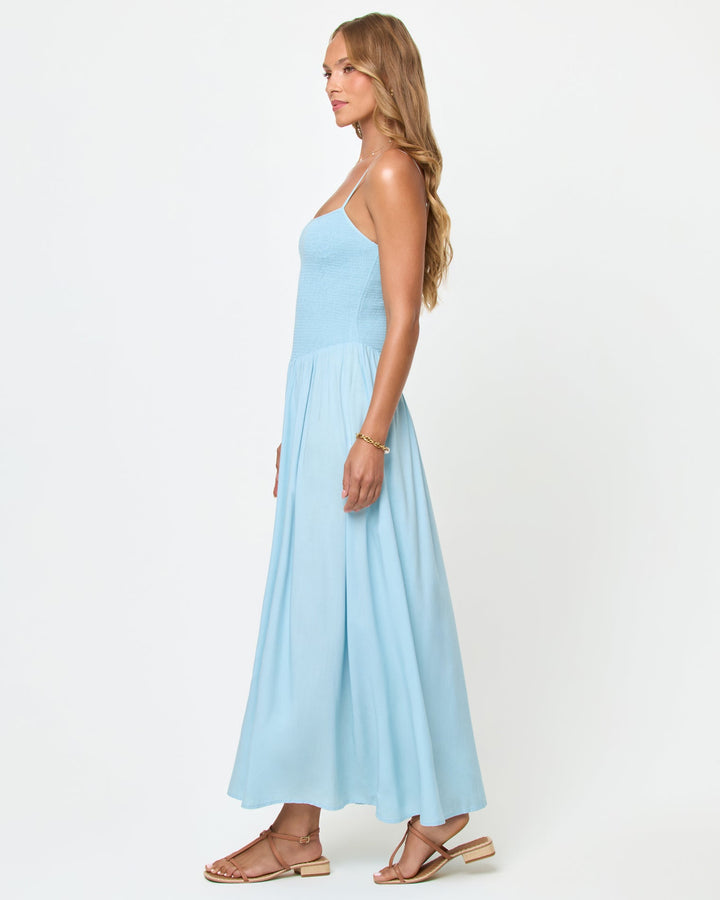 Side view of a model wearing the LSPACE Misha Midi in Tourmaline, showing the silhouette of the smocked bodice and full gathered powder blue midi skirt.