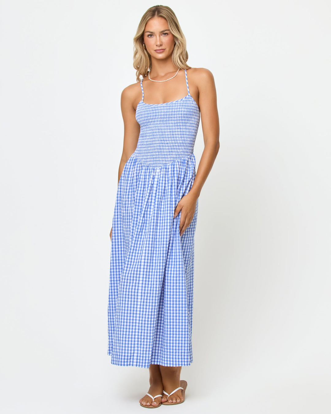 Front view of a model wearing the LSPACE Misha Midi in Morning Gingham, showing the blue and white gingham check pattern, smocked bodice, thin spaghetti straps, and full midi-length skirt.