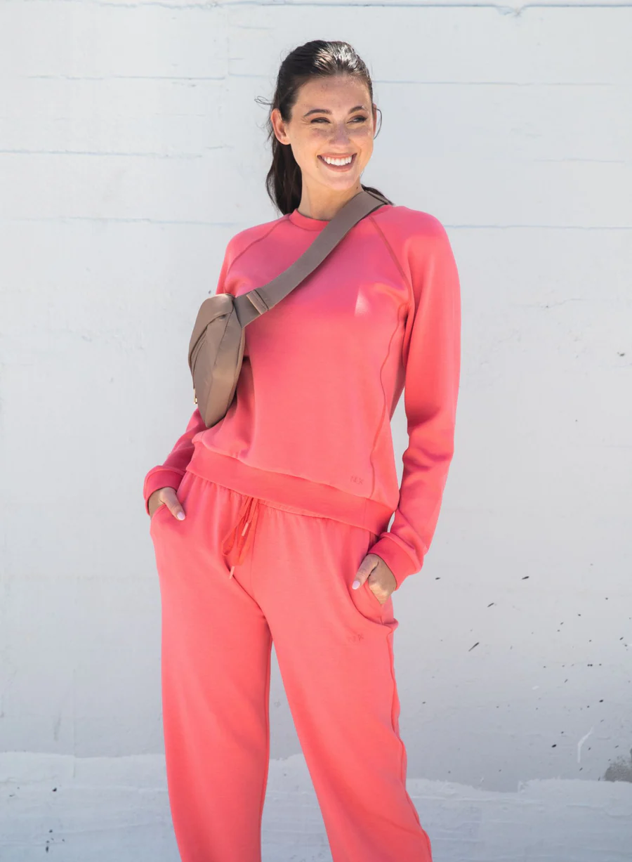 Woman wearing a coral outfit with a beige bag against a light gray background